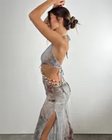 Vestido corto con diseño cut-out en la cintura, escote halter y detalle central de concha marina con cuentas de colores. Presenta un estampado abstracto en tonos azulados y verdosos.