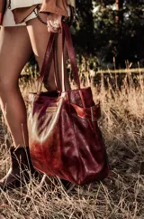 Cartera de cuero color bordó, tipo tote bag, con doble asa de hombro y hebillas decorativas a los costados. Incluye doble bolsillo y colgante interno para llaves.