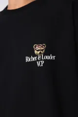 Remera de corte oversize color negro, confeccionada en algodón premium de alto gramaje. Presenta un diseño minimalista con un pequeño estampado frontal que incluye un oso y el texto Richer & Louder VCP.