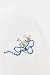 Sudadera de algodón con cuello redondo y manga larga. Presenta un diseño minimalista en color blanco con un delicado bordado de un lazo con flores en el pecho.