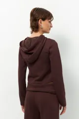 Camperita deportiva color marrón oscuro, ajustada al cuerpo, con capucha y cierre frontal a tono. Presenta costuras verticales que estilizan la figura.