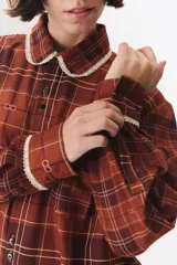 Camisa de corte holgado en color bordó con estampado de cuadros y monograma. Presenta cuello redondo con borde de puntilla, bolsillo frontal con detalle de puntilla, cierre frontal con botones y puños con terminación en puntilla.