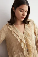 Blusa color beige de manga larga, con escote en V adornado con volados y cierre frontal con botones.