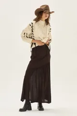 Falda larga de punto en color marrón, confeccionada en una mezcla de viscosa y lurex. Presenta un diseño de corte asimétrico con un volado en el bajo que aporta movimiento y ligereza a la prenda.