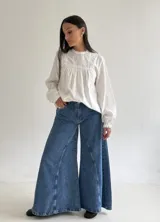 Blusa blanca de corte holgado con cuello redondo, mangas largas con puños elásticos y detalles de puntillas verticales en el frente.