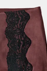 Falda mini de tejido satinado color bordó, con detalle de encaje negro en el frente y bajo asimétrico con abertura.