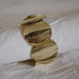 Brazalete rígido dorado con apliques circulares texturizados.