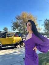 Vestido violeta con escote cuadrado, mangas largas abullonadas, corte ajustado y detalle drapeado con lazo en la cintura.