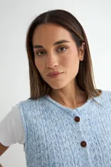 Chaleco de punto color crema con textura tejida, cierre frontal con botones oscuros y cuello redondo.