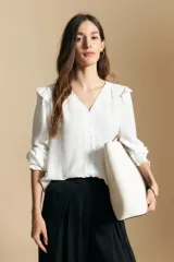 Camisa negra de manga larga con escote en V y cierre frontal de botones. Presenta detalles de volados en los hombros, frunces en la espalda y puños elastizados que le otorgan una silueta relajada y fluida.