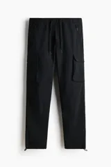 Pantalón cargo negro de nylon, de corte regular con cintura elástica ajustable con cordón. Cuenta con bolsillos laterales con cierre, bolsillos cargo con solapa en las piernas, bolsillos traseros con cierre y tensores en los tobillos.