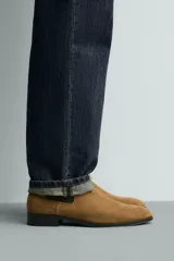 Bota estilo Chelsea fabricada en piel con acabado de serraje, cuenta con elásticos laterales para facilitar el calce, horma redonda y suela a contraste con un ligero tacón.
