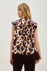 Camisa sin mangas con cuello camisero y botones frontales, confeccionada en tela estampada con patrón animal print en tonos blanco, marrón y azul oscuro.