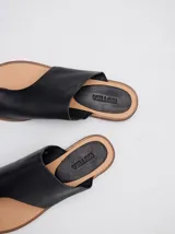 Sandalias planas de cuero color marrón, con diseño minimalista que sujeta el dedo pulgar y deja el empeine al descubierto.
