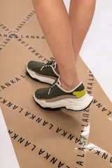 Championes urbanos de cuero verde con textura reptil, detalles en beige y amarillo, cordones negros y suela chunky blanca con base negra.