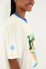 Camiseta blanca de algodón con cuello redondo azul, manga corta y gran estampado frontal con la palabra BRASIL, la bandera de Brasil y un pájaro verde en vuelo.