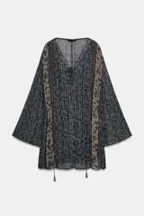 Vestido corto con estampado floral en tonos azul oscuro y beige, con detalles en hilo metalizado. Presenta escote pico con cordón ajustable terminado en borlas, mangas largas acampanadas y cintura elástica ajustable.