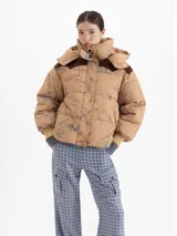 Campera puffer color tostado con estampado de figuras esquiando, capucha desmontable, recortes en corderoy marrón en los hombros, puños tejidos y cierre frontal con botones a presión.