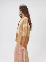 Cardigan oversize de tejido de punto grueso con diseño de bloques de color en tonos tierra. Presenta cuello en V, cierre frontal con botones, mangas largas con terminación abullonada y parches decorativos en el pecho y hombro.