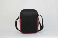 Morral pequeño tipo bandolera, color negro, con detalles en rojo y azul en el frente. Presenta el logo de la NBA en la parte superior y un bolsillo frontal con cierre. Incluye correa regulable.