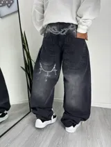 Pantalón de jean estilo baggy con lavado desgastado en color negro. Presenta un diseño estampado con cadenas y cruces en la parte trasera, incluyendo la zona de la cintura y los bolsillos.