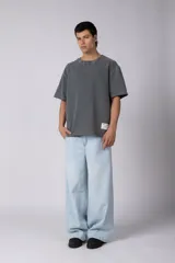 Remeron de corte oversized con cuello redondo y mangas cortas. Presenta un acabado de tela con efecto desgastado y costuras visibles en los bordes, con una etiqueta pequeña en el lateral inferior.