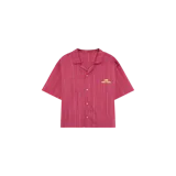 Camisa de manga corta tipo pijama, color rojo con rayas verticales finas, cuello cubano, cierre frontal con botones y dos bolsillos delanteros aplicados. Cuenta con el logotipo de la marca bordado en el pecho.