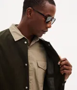Campera bomber masculina de terciopelo cotelé color beige, con cuello redondo, mangas largas, cierre frontal de botones forrados, bolsillos laterales y terminaciones de elástico en puños y cintura.