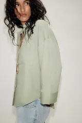 Camisa oversize color verde menta, con cuello camisero, cierre frontal de botones, bolsillo de parche en el pecho y mangas anchas por debajo del codo.