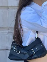 Bolso tipo baguette de cuero sintético negro con múltiples hebillas plateadas.