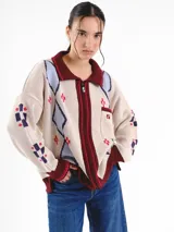 Campera tejida en jacquard con diseño de rombos argyle, cuello mao, cierre frontal y bolsillo ojal en el pecho. Presenta terminaciones en tono burdeos.