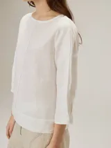 Blusa de algodón color marrón, con escote redondo, mangas tres cuartos con volumen sutil y costuras verticales decorativas en el frente.