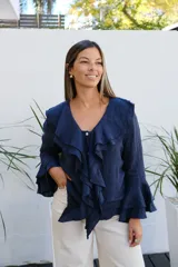 Blusa de lino color azul marino, con cuello con volados, cierre frontal con botones y mangas largas con puños acampanados de doble volado.