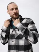 Sobrecamisa de estilo leñador con estampado de cuadros en tonos gris, negro y blanco. Presenta cierre frontal con cremallera y solapa con botones a presión, cuello clásico y bolsillos laterales.