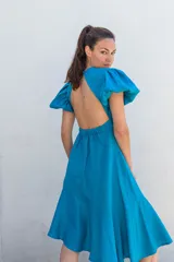 Vestido azul con escote redondo, mangas cortas abullonadas con elástico, espalda descubierta y largo asimétrico.