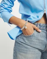 Pulsera de bolas medianas bañadas en plata de ley, con un dije grande en forma de gota y cierre de mosquetón con un pequeño charm grabado.