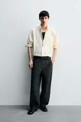 Camisa de algodón color crema o blanco roto, de corte regular fit, con cuello solapa, manga larga con puño abotonado y bolsillo plastrón en el pecho. La tela presenta una textura sutil de rayas verticales en relieve.