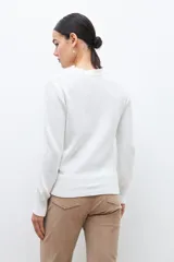 Sweater blanco de punto con bordado de flores azules, rojas y blancas. Tiene cuello redondo y mangas largas.