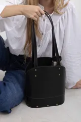Cartera matera de cuero vacuno negro con textura símil lagarto, diseño estructurado con base ovalada y doble asa de hombro. Cuenta con detalles de tachas metálicas doradas y costuras pespunteadas en contraste.
