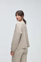 Cardigan de tejido de punto con textura, silueta boxy y cuello en V. Presenta cierre frontal con botones y detalles de terminación en contraste de color en los bordes.