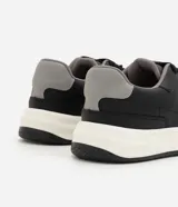 Championes urbanos estilo skate de color negro con suela bicolor blanca y negra, talón gris y detalles perforados en la puntera.