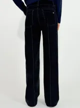 Pantalon de corte recto y tiro medio, confeccionado en denim con acabado aterciopelado en tono marrón oscuro. Presenta costuras verticales marcadas en contraste y cierre frontal con botón y cremallera.