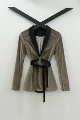 Blazer tipo smoking de terciopelo negro con acabado brillante y detalles estampados en dorado. Presenta solapas clásicas, cierre frontal cruzado mediante un lazo y mangas largas con cierres incorporados. El diseño es entallado y sofisticado.