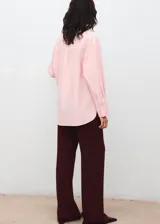 Camisa oversize color rosado, con cuello camisero, manga larga con puños abotonados, bolsillo de parche en el pecho y cierre frontal con botones ocultos.