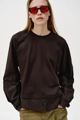 Camiseta oversize de cuello redondo y manga larga con puños abotonados. Confeccionada en algodón, presenta un diseño con combinación de tejidos a tono y bajo asimétrico.