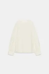 Blusa de cuello redondo y manga larga acabada en puño con frunces, detalle de aberturas en las mangas, frunces laterales y cierre trasero con abertura y botón.
