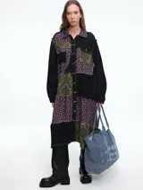 Kimono largo tipo vestido camisero con diseño patchwork que combina paneles de denim negro, tela con estampado floral y tela con estampado damasco en tonos verde oliva y negro. Presenta cierre frontal con botones, cuello camisero y mangas largas.