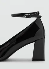 Zapato de tacón cuadrado en charol negro, con punta cuadrada y tira ajustable al tobillo con hebilla.