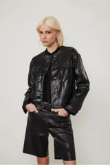 Campera negra efecto vinilo con terminación brillante y cuello redondo acanalado. Presenta bolsillos con solapa en el frente, costuras marcadas y cierre con broches a tono.