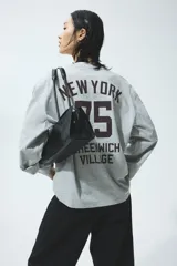 Top oversized de punto de algodón suave en color gris melange, con diseño estampado de letras pequeñas en el pecho. Presenta manga larga, cuello redondo ribeteado y hombros caídos.